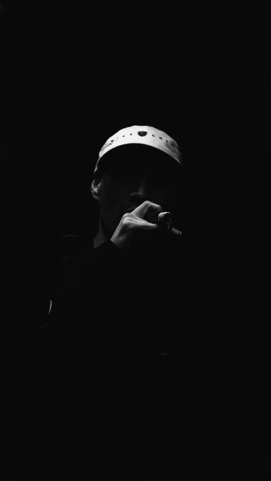 Sin1Rostro cantando con gorra, en la oscuridad